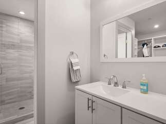 This modern bathroom features a sleek vanity with a white countertop and chrome fixtures, complemented by a spacious walk-in shower with elegant gray tilework.