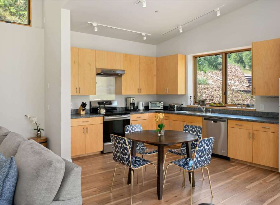 This modern kitchen features light wood cabinetry and sleek countertops, complemented by a round dining table with stylish patterned chairs.