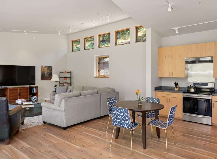Experience modern living in this open-concept space featuring a sleek kitchen with light wood cabinetry and stainless steel appliances, adjacent to a cozy dining area with stylish patterned chairs.