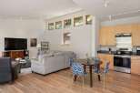 Experience modern living in this open-concept space featuring a sleek kitchen with light wood cabinetry and stainless steel appliances, adjacent to a cozy dining area with stylish patterned chairs.