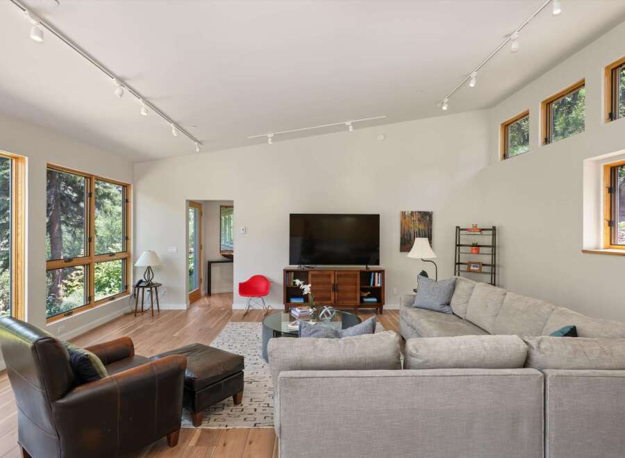 Experience modern living in this stunning living room, featuring a vaulted ceiling with track lighting and expansive windows that flood the space with natural light.