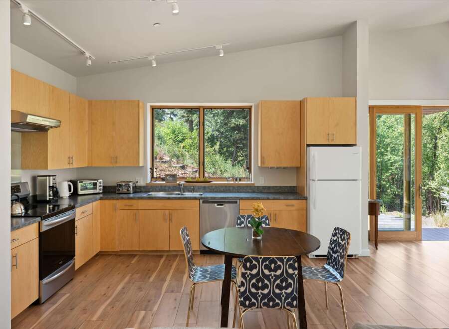 This modern kitchen features light wood cabinetry and sleek countertops, complemented by a large window offering a view of lush greenery.