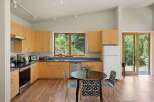 This modern kitchen features light wood cabinetry and sleek countertops, complemented by a large window offering a view of lush greenery.
