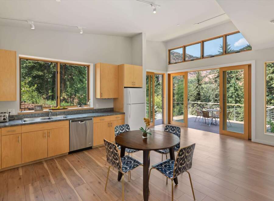 Experience seamless indoor-outdoor living in this stunning kitchen and dining area, featuring expansive windows and glass doors that open to a scenic deck with mountain views.