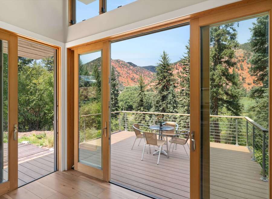 Experience seamless indoor-outdoor living with expansive sliding glass doors that open onto a spacious deck, offering breathtaking views of the surrounding red rock mountains and lush greenery.