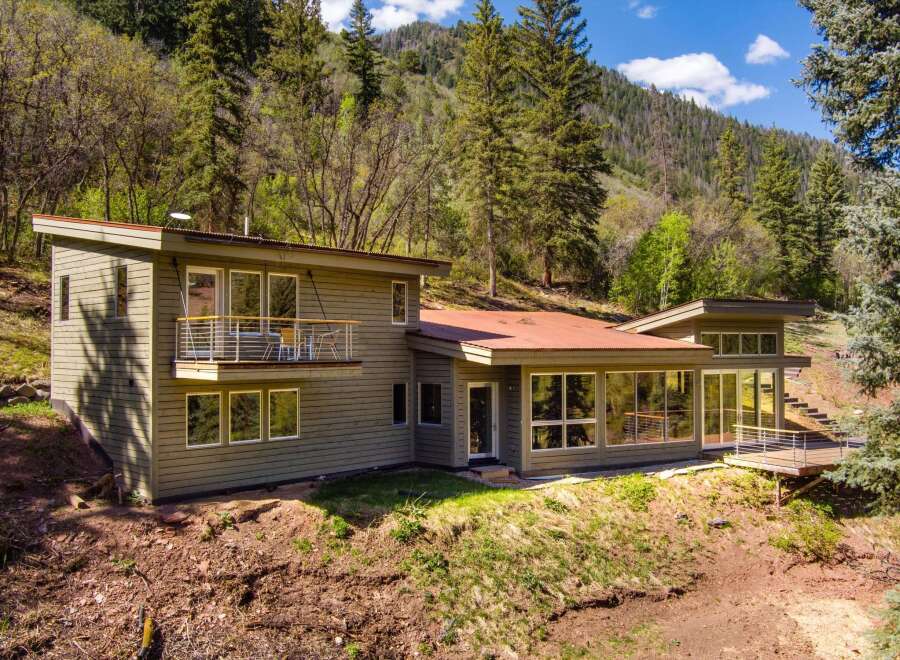 Nestled amidst a lush forest, this modern home offers a serene retreat with its expansive windows and natural wood siding.