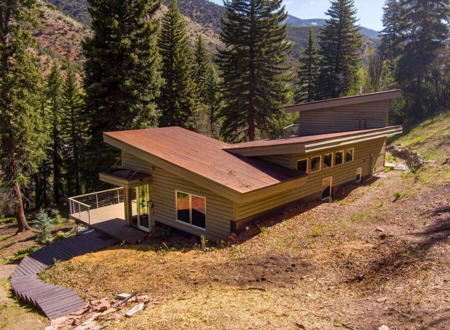 Nestled amidst a serene forest, this modern home offers a unique architectural design with a striking corrugated metal roof and natural wood siding.