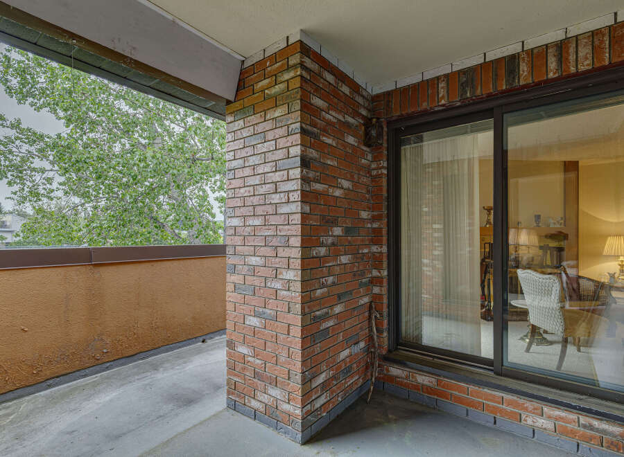 Enjoy the outdoors from this charming balcony, featuring a classic brick accent wall and a large sliding glass door that opens to a bright interior.