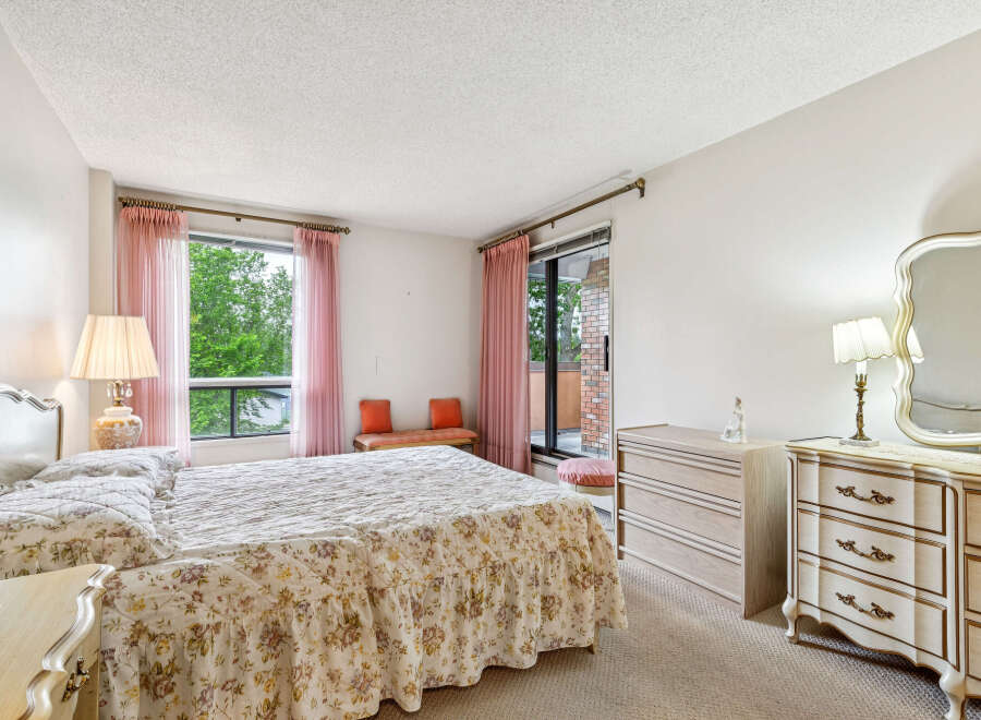 This charming bedroom features a spacious king-size bed adorned with a floral comforter and ruffled skirt, complemented by elegant pink sheer curtains.