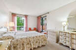 This charming bedroom features a spacious king-size bed adorned with a floral comforter and ruffled skirt, complemented by elegant pink sheer curtains.
