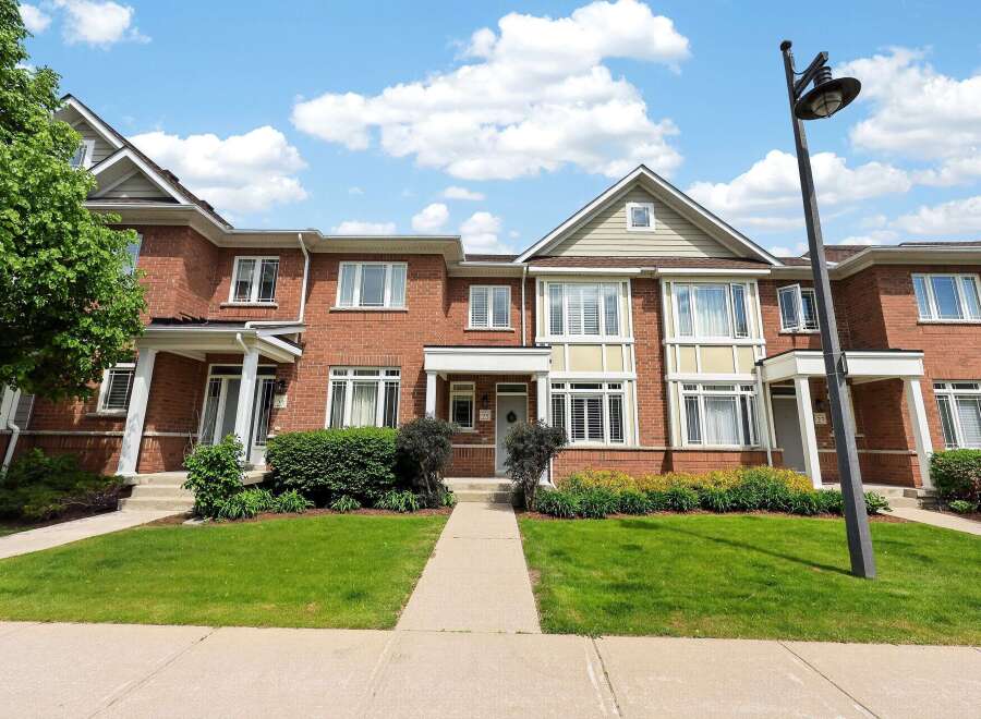 Discover this charming brick townhouse offering a welcoming facade with a well-maintained lawn and garden beds.