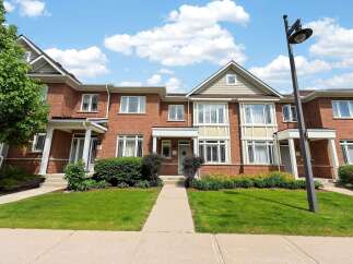 Discover this charming brick townhouse offering a welcoming facade with a well-maintained lawn and garden beds.