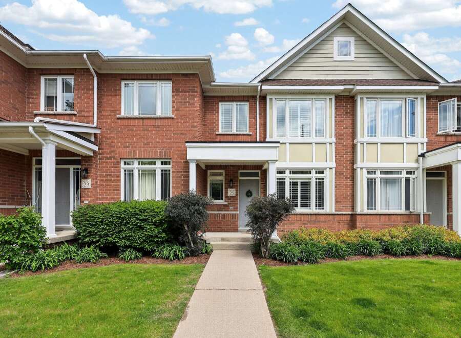 Charming brick townhouse featuring a welcoming covered porch and a well-maintained front lawn.