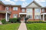 Charming brick townhouse featuring a welcoming covered porch and a well-maintained front lawn.
