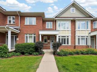 Charming brick townhouse featuring a welcoming covered porch and a well-maintained front lawn.
