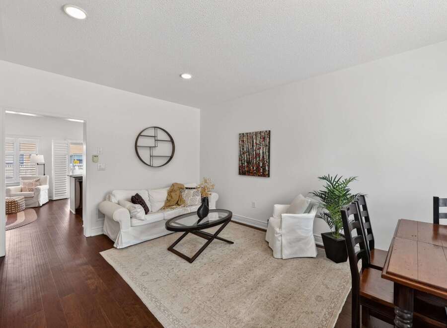 Step into this inviting living space featuring a comfortable white sofa adorned with decorative pillows and a cozy throw, complemented by a stylish glass-top coffee table.