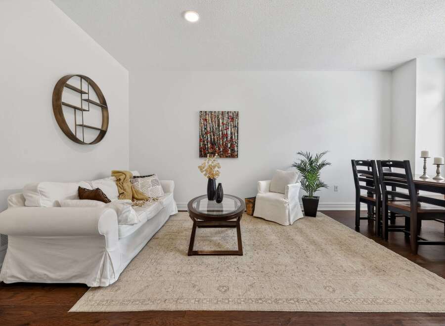 This inviting living space features a comfortable white slipcovered sofa adorned with throw pillows and blankets, complemented by a round glass-top coffee table.