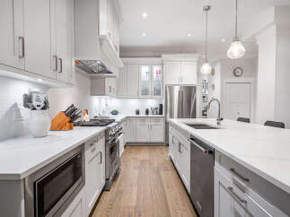 Experience luxury in this stunning modern kitchen, boasting sleek white cabinetry, a spacious quartz island with a built-in sink, and top-of-the-line stainless steel appliances.
