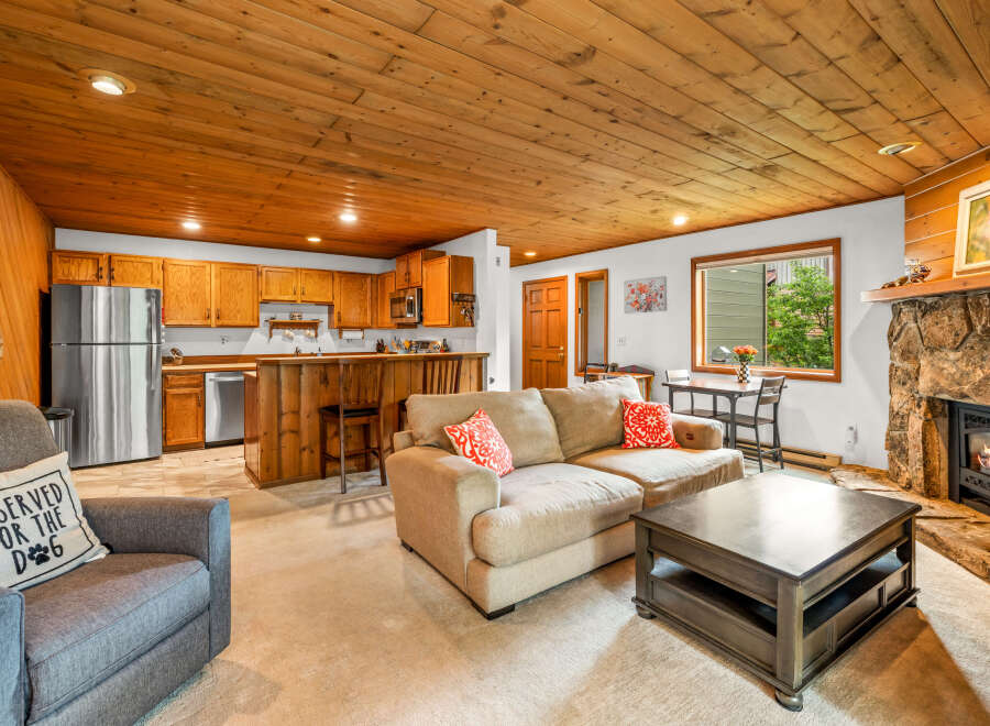 Cozy living room featuring a natural stone fireplace and a warm, wood-paneled ceiling.
