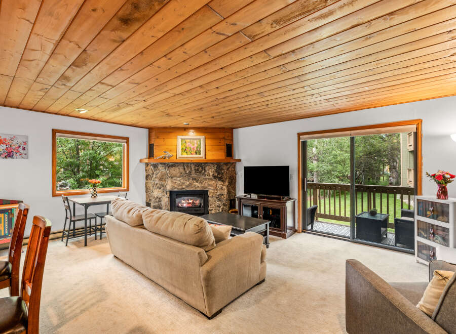Cozy living room featuring a natural stone fireplace and a warm wood-paneled ceiling.