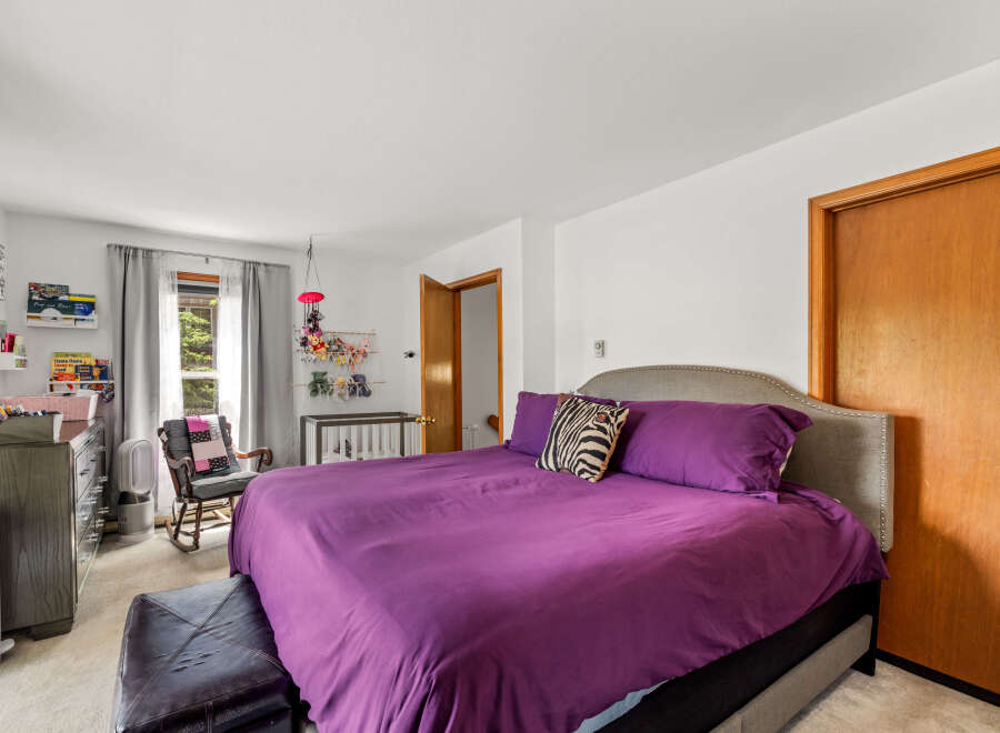 This charming bedroom features a spacious king-size bed with a luxurious purple comforter and a stylish upholstered headboard.