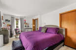 This charming bedroom features a spacious king-size bed with a luxurious purple comforter and a stylish upholstered headboard.