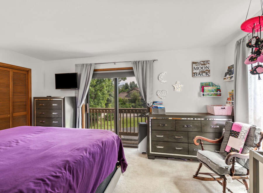 Discover a charming bedroom featuring a comfortable bed with a vibrant purple comforter, complemented by a dark wood dresser and a mounted television.