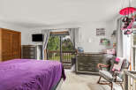 Discover a charming bedroom featuring a comfortable bed with a vibrant purple comforter, complemented by a dark wood dresser and a mounted television.