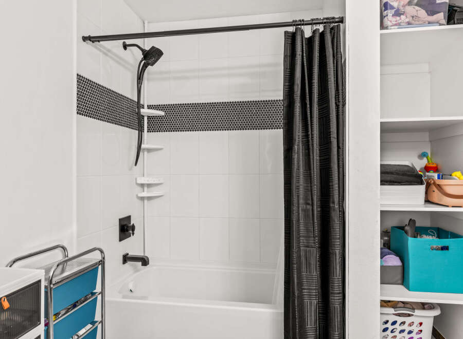 This bathroom features a clean white tiled shower and tub combination, accented by a stylish black mosaic tile band.