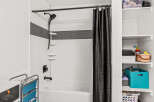 This bathroom features a clean white tiled shower and tub combination, accented by a stylish black mosaic tile band.