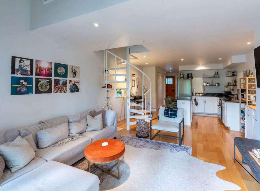 This stylish open-concept living space features a comfortable sectional sofa adorned with plush pillows, complemented by a vibrant orange ottoman coffee table.
