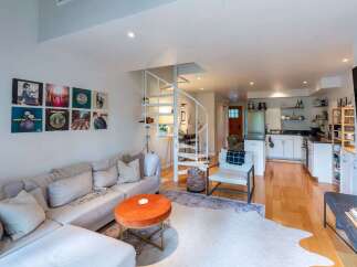 This stylish open-concept living space features a comfortable sectional sofa adorned with plush pillows, complemented by a vibrant orange ottoman coffee table.