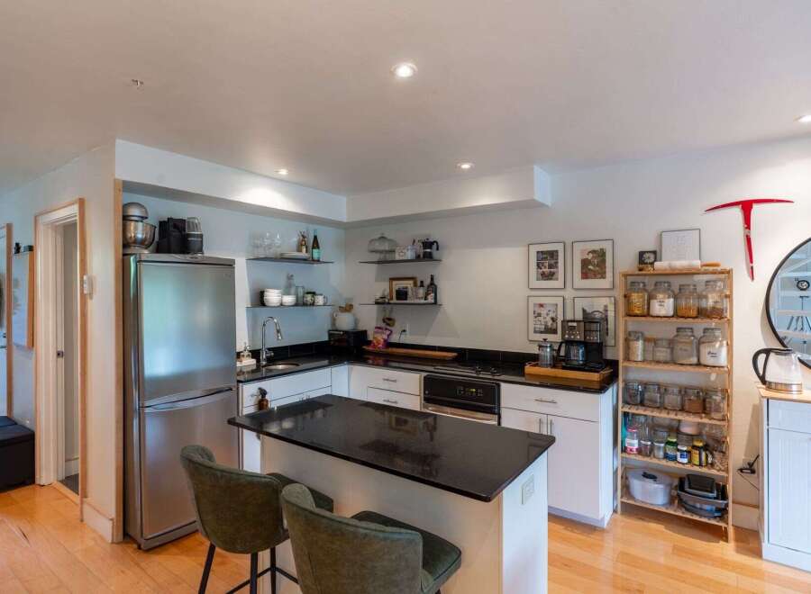This modern kitchen boasts a sleek granite countertop island, perfect for meal prep and casual dining with its two accompanying bar stools.