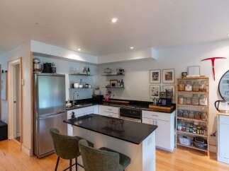 This modern kitchen boasts a sleek granite countertop island, perfect for meal prep and casual dining with its two accompanying bar stools.