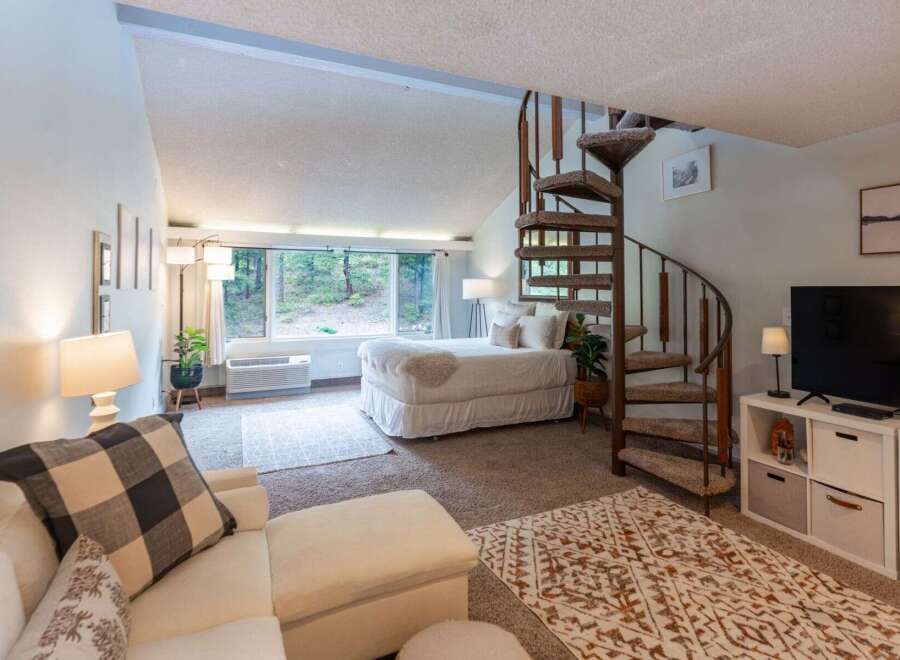 Discover this charming studio apartment featuring a cozy bed area with large windows offering serene forest views.