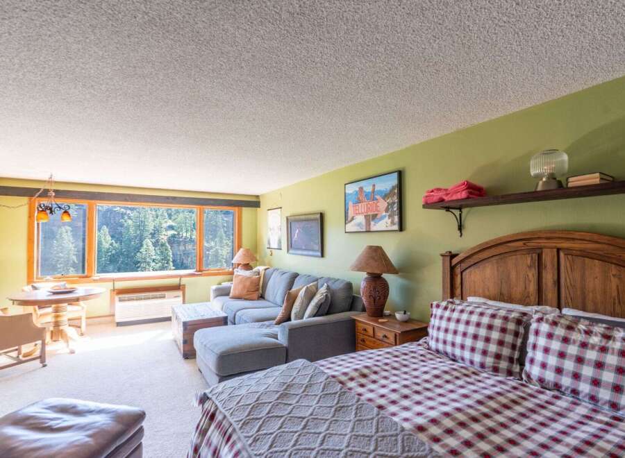 Experience breathtaking mountain views from this charming studio apartment, featuring a cozy living area with a sectional sofa and a comfortable queen-size bed.
