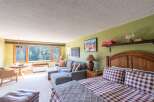 Experience breathtaking mountain views from this charming studio apartment, featuring a cozy living area with a sectional sofa and a comfortable queen-size bed.
