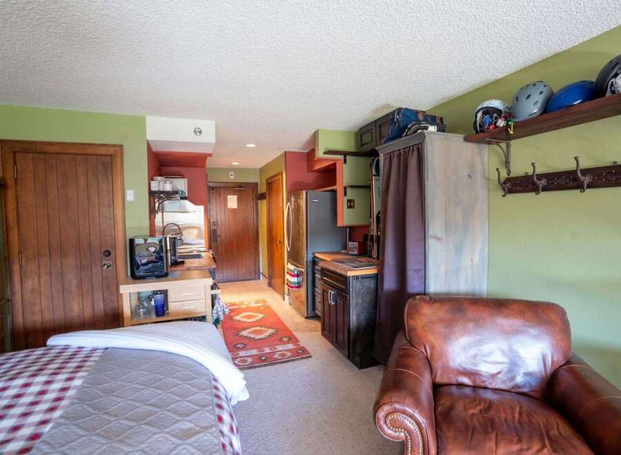 Discover this charming studio apartment featuring a cozy sleeping area, a functional kitchenette with a coffee maker, and a comfortable leather armchair perfect for relaxing.