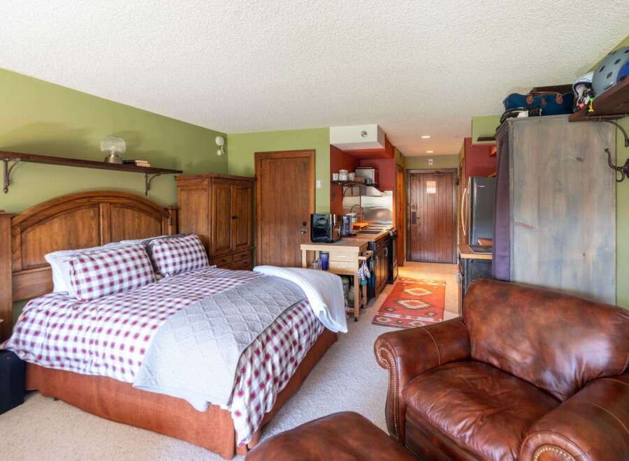 Experience cozy living in this charming studio apartment, featuring a comfortable queen-size bed with plaid bedding and a convenient kitchenette.