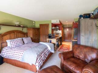 Experience cozy living in this charming studio apartment, featuring a comfortable queen-size bed with plaid bedding and a convenient kitchenette.