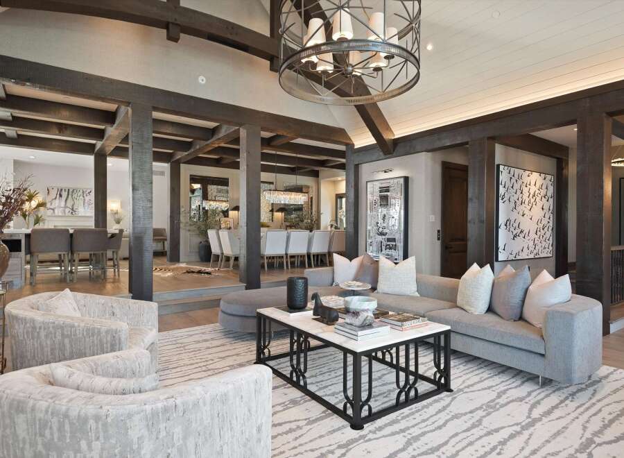 Experience luxurious living in this stunning open-concept great room, featuring exposed wooden beams and a grand chandelier.