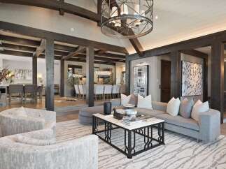 Experience luxurious living in this stunning open-concept great room, featuring exposed wooden beams and a grand chandelier.