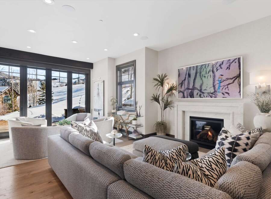 Experience luxury mountain living in this stunning living room, featuring a cozy fireplace and expansive windows that showcase breathtaking snowy vistas.