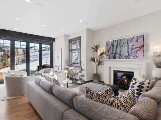 Experience luxury mountain living in this stunning living room, featuring a cozy fireplace and expansive windows that showcase breathtaking snowy vistas.