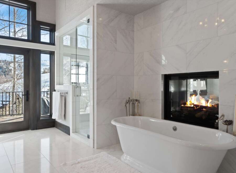 Experience luxury in this stunning bathroom featuring a freestanding soaking tub positioned perfectly to enjoy the ambiance of a modern fireplace.