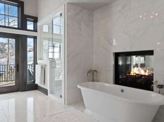 Experience luxury in this stunning bathroom featuring a freestanding soaking tub positioned perfectly to enjoy the ambiance of a modern fireplace.