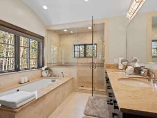 Indulge in luxury in this stunning bathroom featuring a deep soaking tub with a picturesque window view and a spacious glass-enclosed shower.