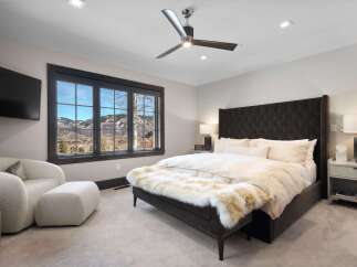Experience luxury mountain living in this stunning bedroom, featuring a plush tufted headboard and a cozy seating area with a view.