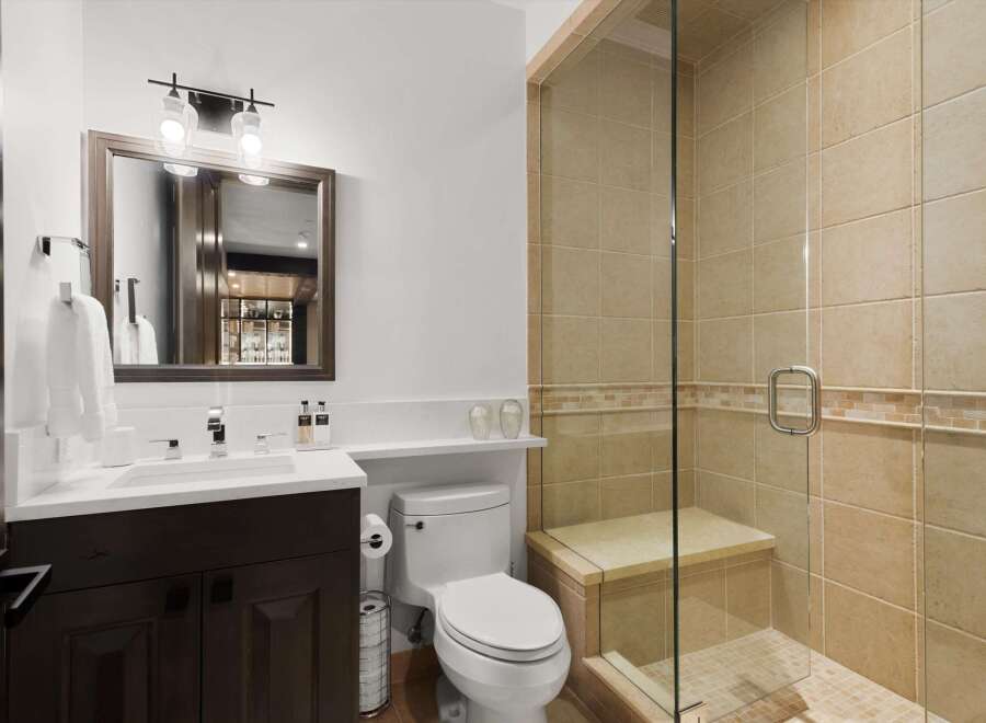 This modern bathroom features a sleek vanity with a white countertop and dark wood cabinetry, complemented by a stylish chrome faucet.