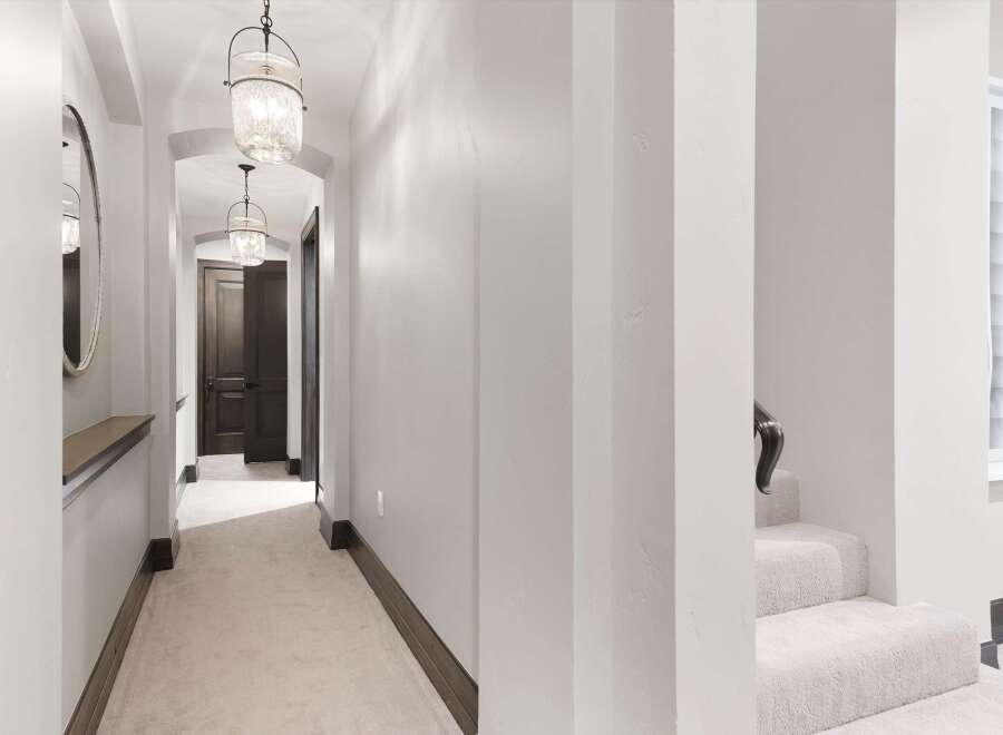 Step into this elegant hallway featuring a plush carpet and sophisticated pendant lighting that guides you towards dark wood doors.